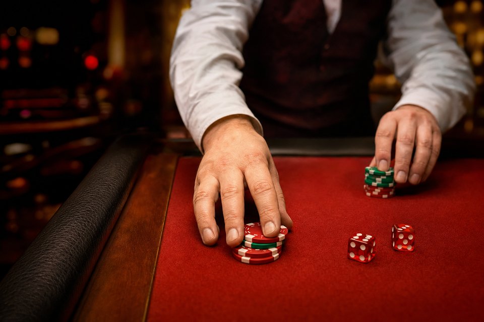 A craps dealer pushing stacks of red and green chips across the rail toward the camera (AI-generated image)