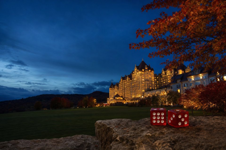A casino resort in upstate New York at twilight, its lit windows glowing across a wide lawn with autumn trees (AI-generated image)