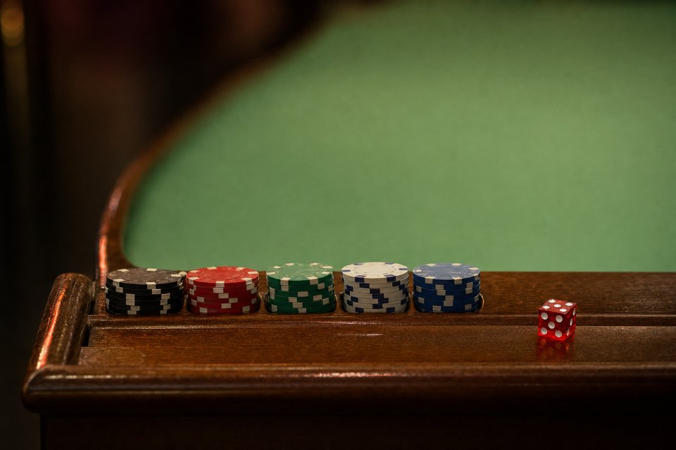 Five short stacks of chips lined up in the rail groove of a craps table, with one red die beside them (AI-generated image)